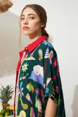 Túnica de manga corta con cuello verde oscuro y solapas a rayas verticales en tonos rosado, azul y rojo. El cuerpo principal es de color crema con un estampado colorido de estilo veraniego y tropical.