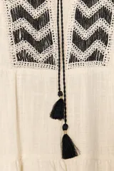 Vestido corto color crudo con escote en pico con cordón con borlas y manga larga. Presenta bordados en el frente.