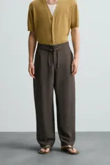 Pantalón marrón de corte ancho, con cintura ajustable con cordón, bolsillos delanteros y traseros tipo parche, detalle de costuras verticales en el frente y cierre frontal con cremallera y gancho metálico oculto.