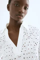Camisa blanca de algodón con broderie, corte holgado, cuello abierto, mangas anchas al codo y ribete festoneado en mangas y bajo.