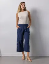 Pantalón blanco de algodón con pretina elastizada, bolsillos inclinados y ruedo lateral con tajo y botones.