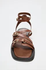 Sandalias planas de cuero color marrón con tiras finas y hebillas doradas.