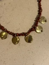 Collar corto con cuentas de piedras de colores y dijes de monedas de bronce. Collar largo con cadena dorada y dije de metal.