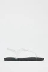 Sandalia plana con tiras de vinilo transparente y suela negra.