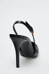 Zapato de tacón fino color negro con efecto relieve en el cuerpo, tira trasera con hebilla ajustable y acabado en punta.