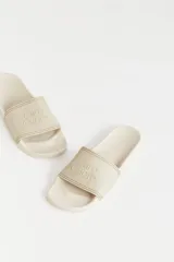 Ojotas de goma color beige con tira ancha sobre el empeine y logo de la marca en relieve.