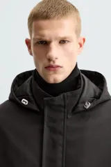 Parka negra de tejido técnico acolchado, corte regular fit, cuello alto con capucha ajustable, manga larga con puños ajustables, bolsillos de solapa en la cadera y bolsillo interior. Cierre frontal con cremallera oculta y botones a presión.