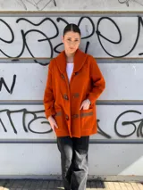 Saco de punto fino color naranja con detalles en tejido grueso y cuero, cierre frontal con botones y cuello amplio.
