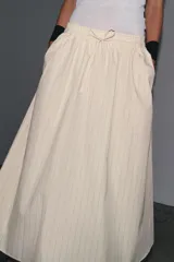Falda midi de Zara Woman Collection confeccionada en hilatura de algodón color crudo con finas rayas verticales marrones. Tiene tiro medio, cintura elástica ajustable con cordones y bajo evasé.