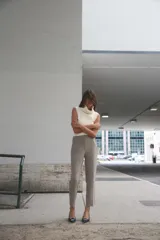 Pantalón tobillero color gris claro, de tiro alto, con bolsillos delanteros de vivo y cierre frontal con cremallera, botón interior y gancho metálico.