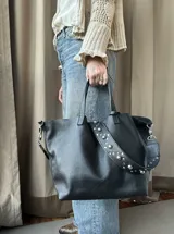 Cartera tipo tote bag color bordó, confeccionada en cuero con textura granulada. Tiene doble asa corta de mano y asa larga extraíble con diseño de tachas para usar como bandolera.