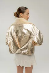 Campera corta dorada de cuero sintético metalizado con cuello de piel sintética color crema, cierre frontal con botones marrones y bolsillos de parche en el pecho.