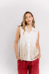 Blusa blanca sin mangas con cuello camisero y bordado dorado con motivos vegetales en la parte inferior.