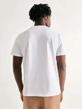 Camiseta blanca de algodón con cuello redondo y mangas cortas. Estampa rectangular con borde negro que contiene la frase "NATURAL ATMOSPHERE" en letras mayúsculas y una imagen de montañas y mar.