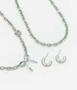 Conjunto de collar y aros plateados con cadena de eslabones gruesos. El collar tiene un dije de lazo y otro de rosa. Los aros son tipo argolla.