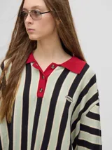 Chomba de corte oversize con cuello camisero, a rayas verticales en color marrón, lila y blanco. Tiene un logo bordado en el pecho y puños en color marrón.