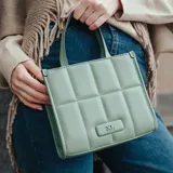 Cartera tote de símil cuero color verde con diseño acolchado y logo metálico XL Extra Large al frente. Tiene acceso con cierre, correa regulable y herrajes plateados. El interior es de tela de algodón y poliéster y cuenta con un bolsillo con cierre y otro abierto.