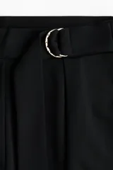 Pantalón sastrero negro de punto con tiro alto, elástico oculto en la cintura y cierre decorativo. Incluye cinturón cosido con anillas en D de metal en un lateral y pinzas para estilizar la silueta.