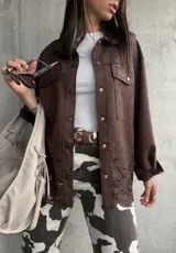Sobrecamisa marrón de gamuza sintética, corte oversize, con cuello camisero, cierre frontal con botones a presión, mangas largas con puños abotonados, bolsillos de parche en el pecho y detalle de calado con motivos florales en el ruedo.