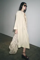 Vestido tipo túnica color crudo con rayas verticales negras, cuello redondo con escote pico ajustable con lazadas y mangas largas.
