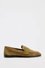 Zapato plano tipo mocasín color marrón claro, confeccionado en piel de serraje. Tiene copete subido, antifaz y punta redonda.