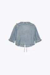 Camisa corta celeste confeccionada en algodón 100%. Presenta cuello bobo con bordados florales, mangas cortas abullonadas y cierre frontal con lazadas.