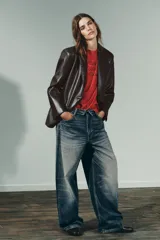 Blazer marrón oscuro de efecto piel, con cuello solapa y manga larga. Tiene bolsillos de plastrón en la parte delantera, forro interior a tono y cierre frontal con botones.