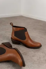 Botín Chelsea de cuero marrón con elástico lateral y tacón bajo.