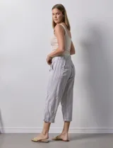 Pantalón capri de lino a rayas verticales en tonos grisáceos y beige, con cintura elástica y lazo ajustable.