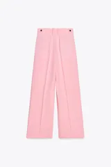 Pantalón rosa de tiro medio con trabillas en la cintura, bolsillos laterales, pinzas delanteras y pierna ancha. Cierre frontal con cremallera, botón y ganchos metálicos.