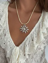 Collar con tiento trenzado color crema y dije de acero quirúrgico hipoalergénico con forma de sol o flor estilizada.