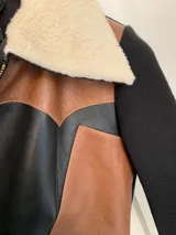 Campera negra con paneles de cuero color marrón, mangas largas de tejido de punto y cuello de piel sintética color crema.