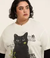 Remera de algodón color crudo, de corte holgado y mangas cortas. Estampado frontal con un gato negro y detalles gráficos en verde y negro.