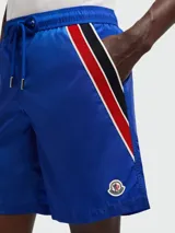 Short de baño azul con cintura elástica y cordón ajustable. Presenta una franja tricolor (rojo, blanco y negro) en el lateral.