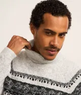 Suéter de punto gris con cuello alto y manga larga. Presenta textura jacquard y estampa horizontal étnica en tonos negros.