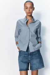 Camisa de cuello solapa y manga tres cuartos con puño ancho. Tiene aberturas laterales en el bajo y cierre frontal con botones ocultos.