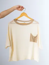 Remera tejida en hilo italiano color crema, con cuello redondo y bolsillo frontal. De corte holgado y silueta amplia.
