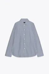 Camisa blanca de popelina de algodón, con cuello solapa y mangas largas con puños abotonados.