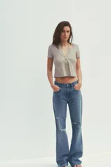 Camiseta color beige de tejido de punto, con cuello halter y escote pico. Tiene cierre frontal con botones y mangas cortas.