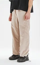 Pantalón beige de corte sastrero con bolsillos laterales, estilo holgado y tela suede. Cintura trasera con doble ajuste elástico y tanca, cintura delantera con botón y cierre.