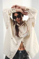 Camisa color crudo a rayas, de corte oversized con hombros caídos y silueta amplia. Presenta un recorte delantero con vivo contrastante, botones al frente y logo bordado al frente.