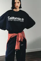 Sudadera azul marino de cuello redondo y manga larga, con texto "California" y diseño gráfico en blanco en el frente.