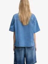 Camisa de denim azul claro de Carhartt WIP, corte relajado, manga corta, cuello camisero, cierre frontal con botones y bolsillo de parche en el pecho con logo de la marca.