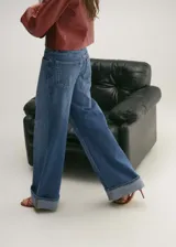Pantalón de jean azul de corte wide leg, tiro medio, con cierre de cremallera y botón, bajo con dobladillo y cinco bolsillos.