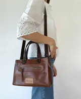 Cartera bandolera de cuero color marrón tostado, con doble asa corta y correa larga desmontable. Tiene un bolsillo frontal con cierre y un bolsillo interno.