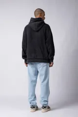 Buzo canguro negro con capucha, calce oversize, confeccionado en frisa 100% algodón con lavado gastado y aplique cosido en el pecho.