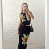 Conjunto de dos piezas negro, compuesto por un top sin mangas ajustado y una falda larga y fluida. Ambas prendas tienen un estampado grande y difuminado de una flor en tonos verde claro y rojo anaranjado.