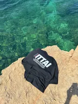 Remera color crema de corte recto y mangas cortas, con estampado en la espalda con el logo "ITTAI" en negro con líneas rojas, azules y blancas, y la leyenda "AN IBIZA PRODUCE. Ittai Stars Department Gallery - Ibiza Edition. If you're in Ibiza, 112 is not an option.".