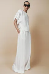 Pantalón palazzo color crudo, confeccionado en hilatura con mezcla de lyocell. Tiro medio, cintura elástica ajustable con cordones, bolsillos laterales ocultos en costura y pierna ancha.