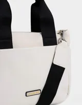 Cartera tipo tote color blanco hueso, con doble asa corta negra y correa larga negra regulable y desmontable. Tiene cierre superior, bolsillos laterales y tag de goma con el logo de la marca.